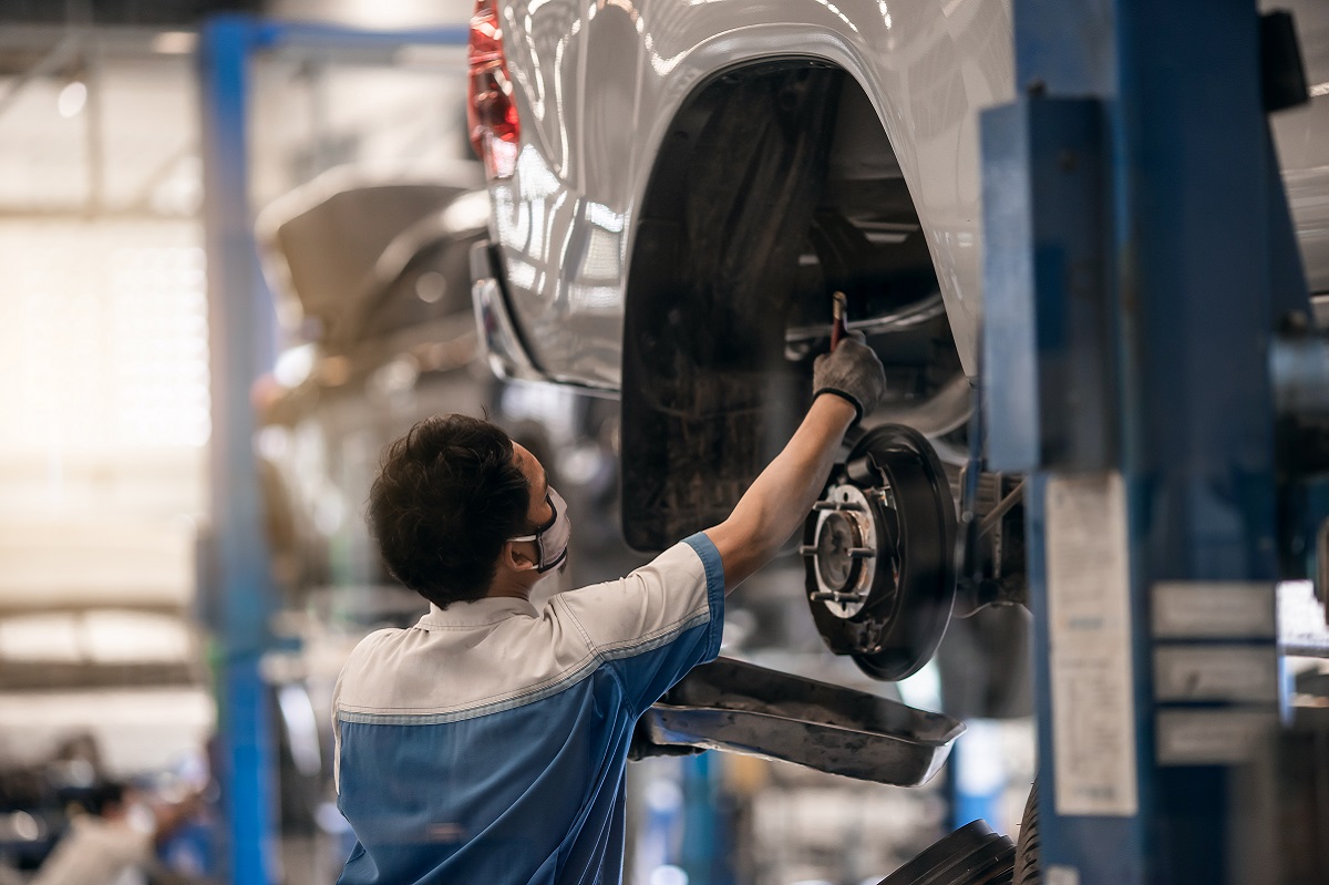 Mechanic inspecting car suspension detail and wheel car of lifted automobile at repair service station. Car service station. Preventive maintenance.