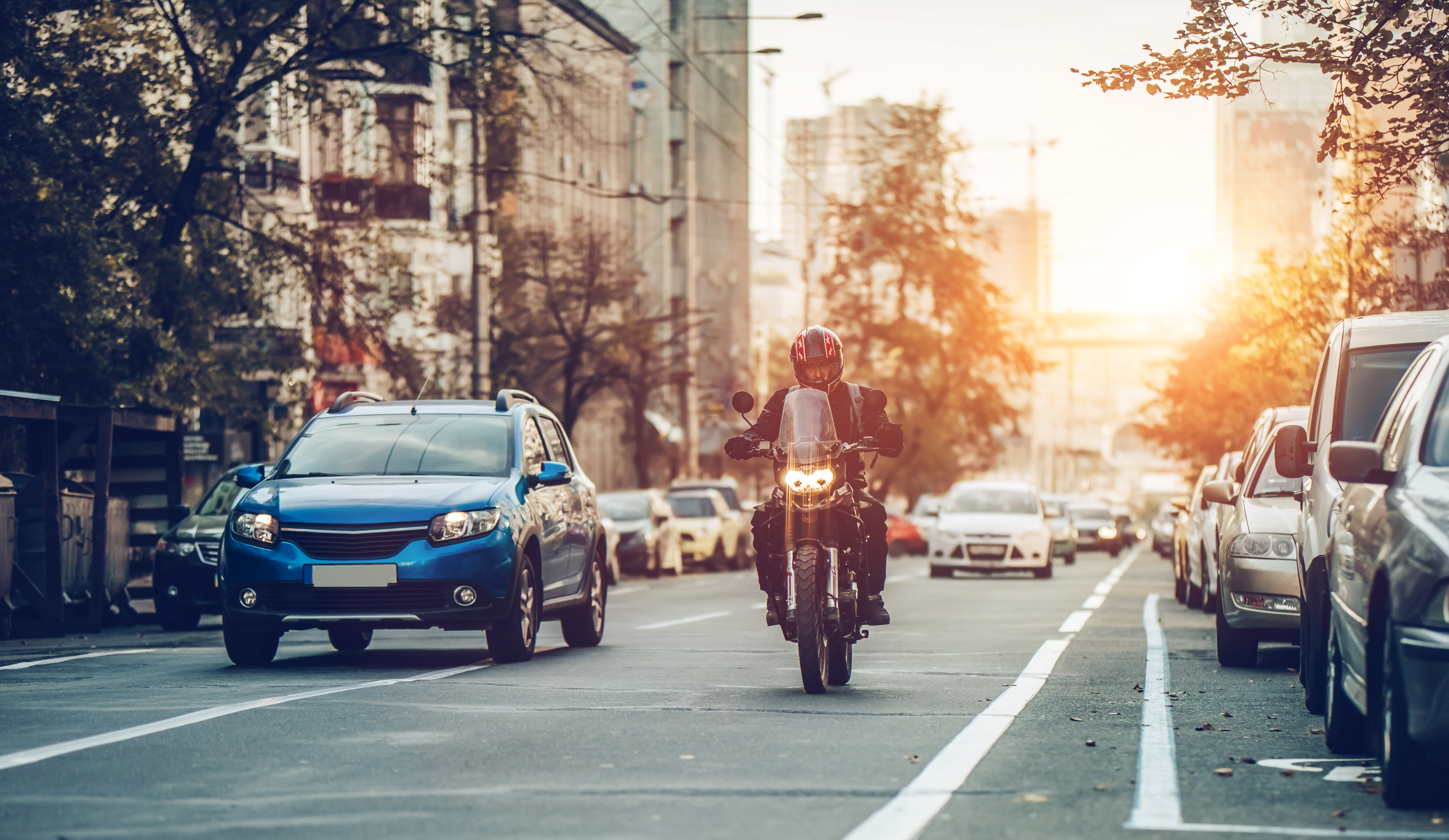 Motorcycle and cars are riding on street. City during the sunset.